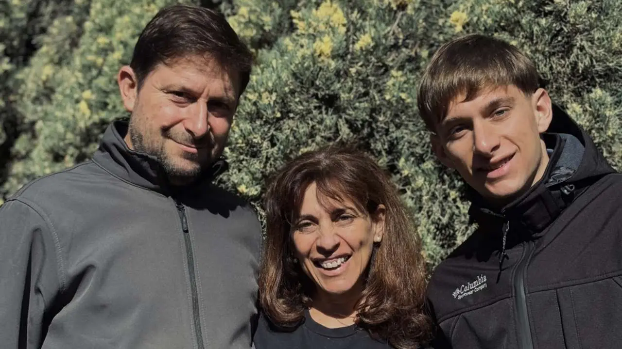 Dario, Viviana y Valetin Burgra, abrazados sonriendo a cámara. Detrás un árbol de nuez pecán