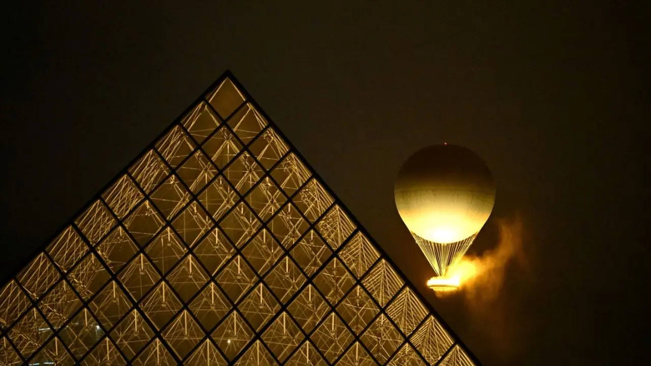 El pebetero olímpico encendido, detrás de la pirámide del Louvre