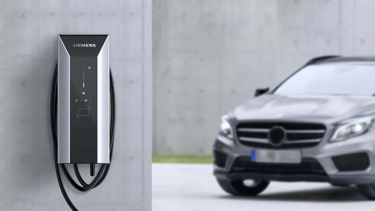 Cargador eléctrico en pared y auto de fondo. Foto oficial.