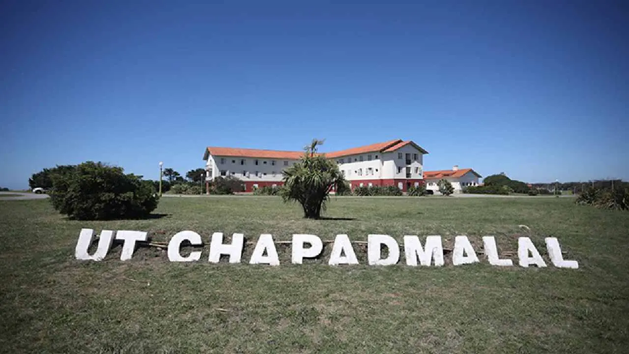 Cartel de acceso a la Unidad Turística Chapadmalal sobre el césped con uno de los hoteles históricos al fondo bajo un cielo despejado