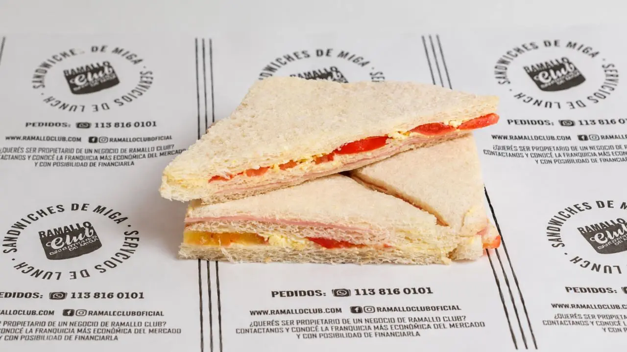 Sobre un mantel promocional de la marca hay tres sándwiches de miga
