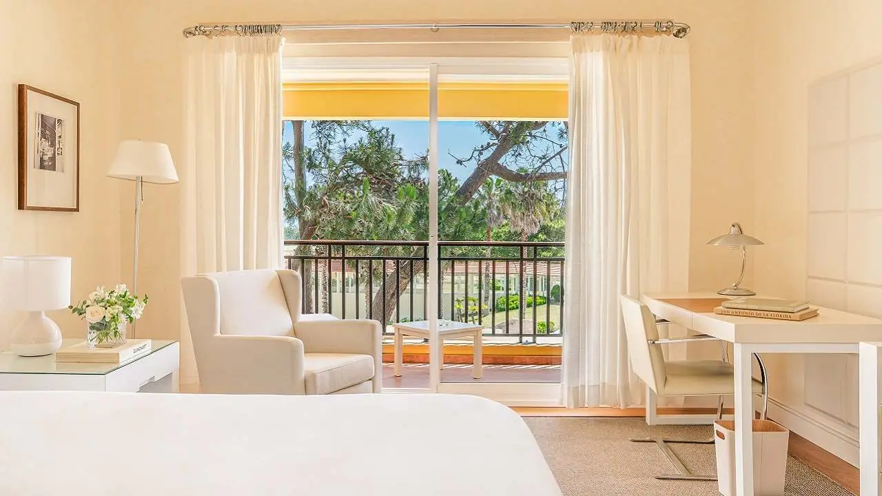 Habitación de un hotel en tonos blanco, beige y madera con ventana hacia un parque