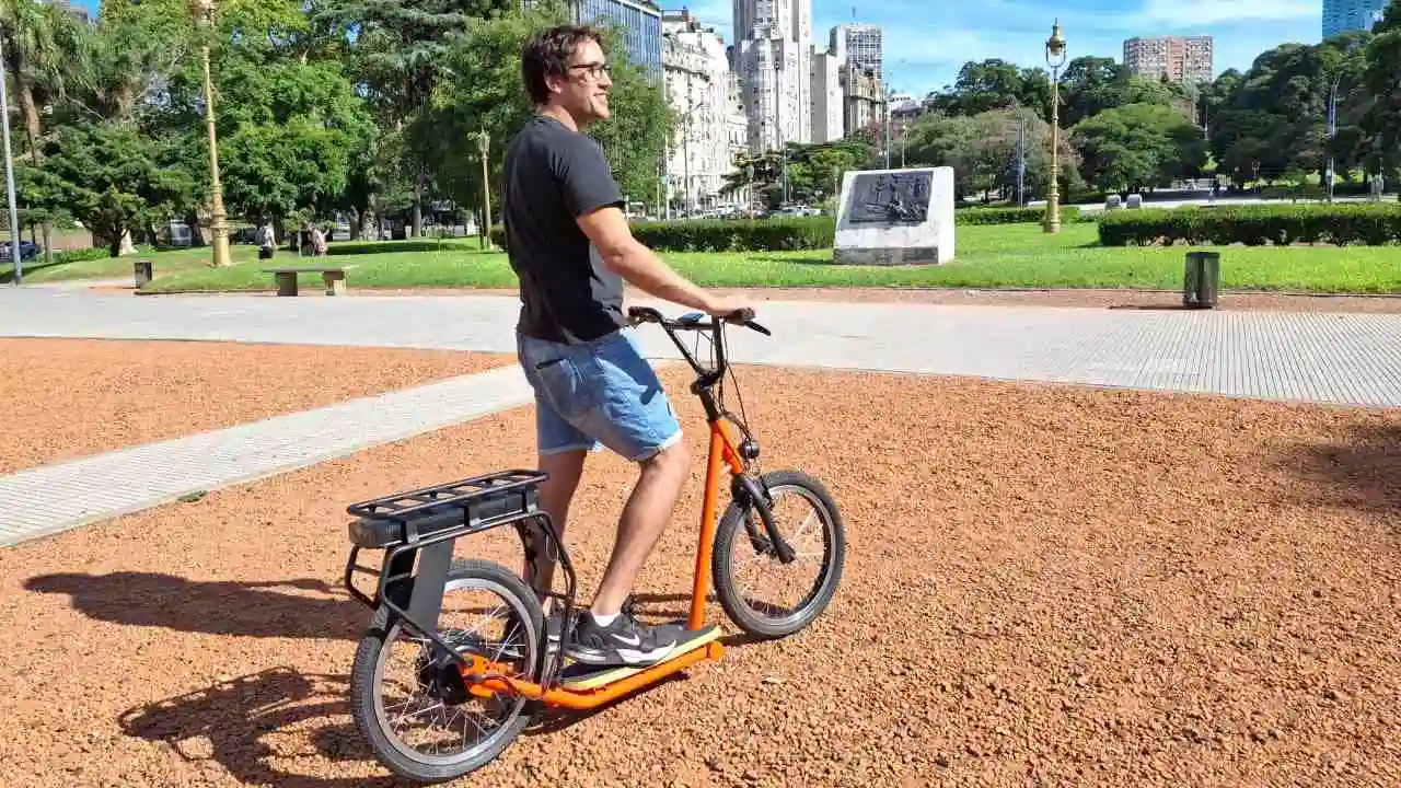 Un turista arriba de una bicipatineta naranja en una plaza del barrio porteño de retiro