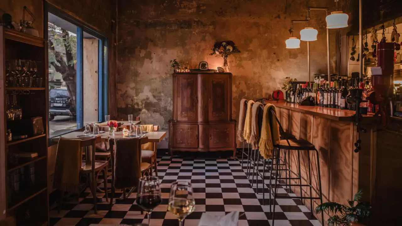 El salón combina paredes rústicas, piso damero y una barra de madera