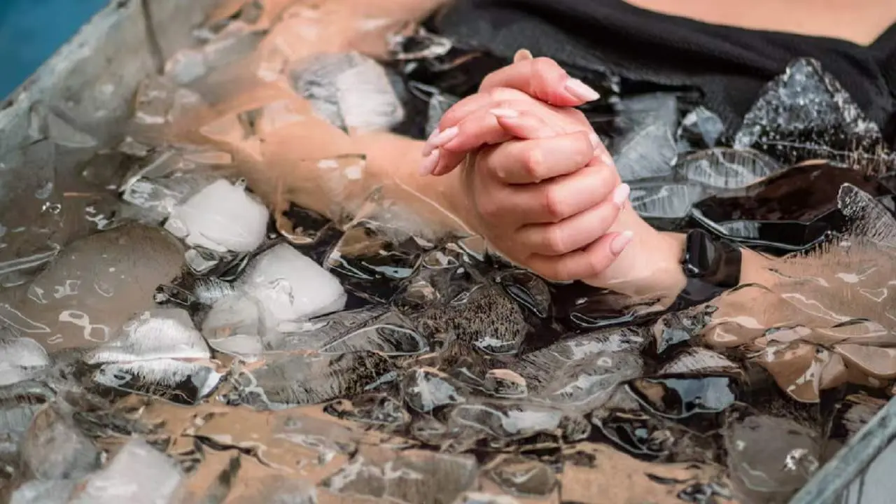 Dos manos de una mujer apretánsode y el resto del cuerpo que se ve en una tina con hielo y agua helada