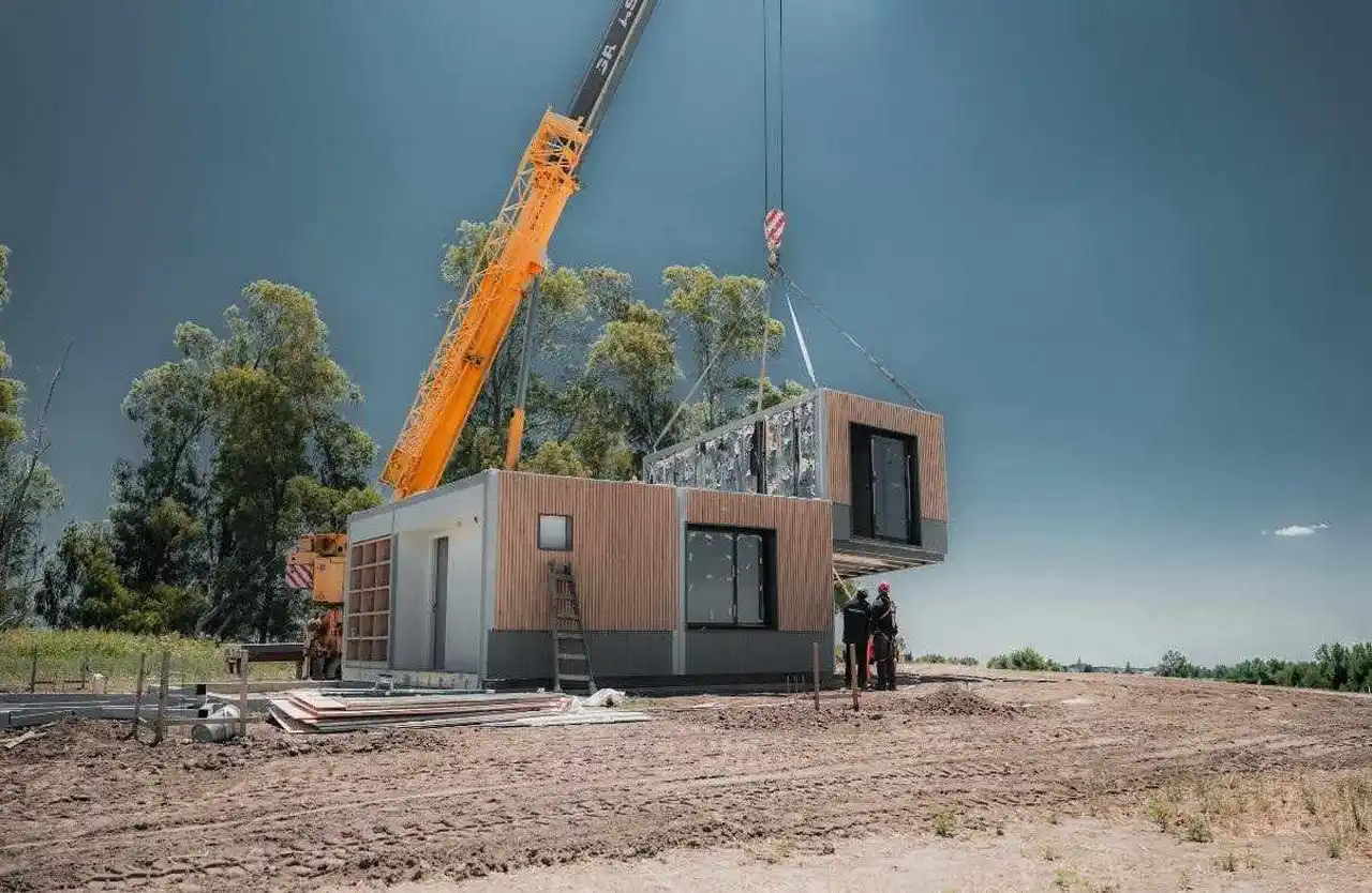 Grúa instala un módulo prefabricado sobre una vivienda modular en construcción.