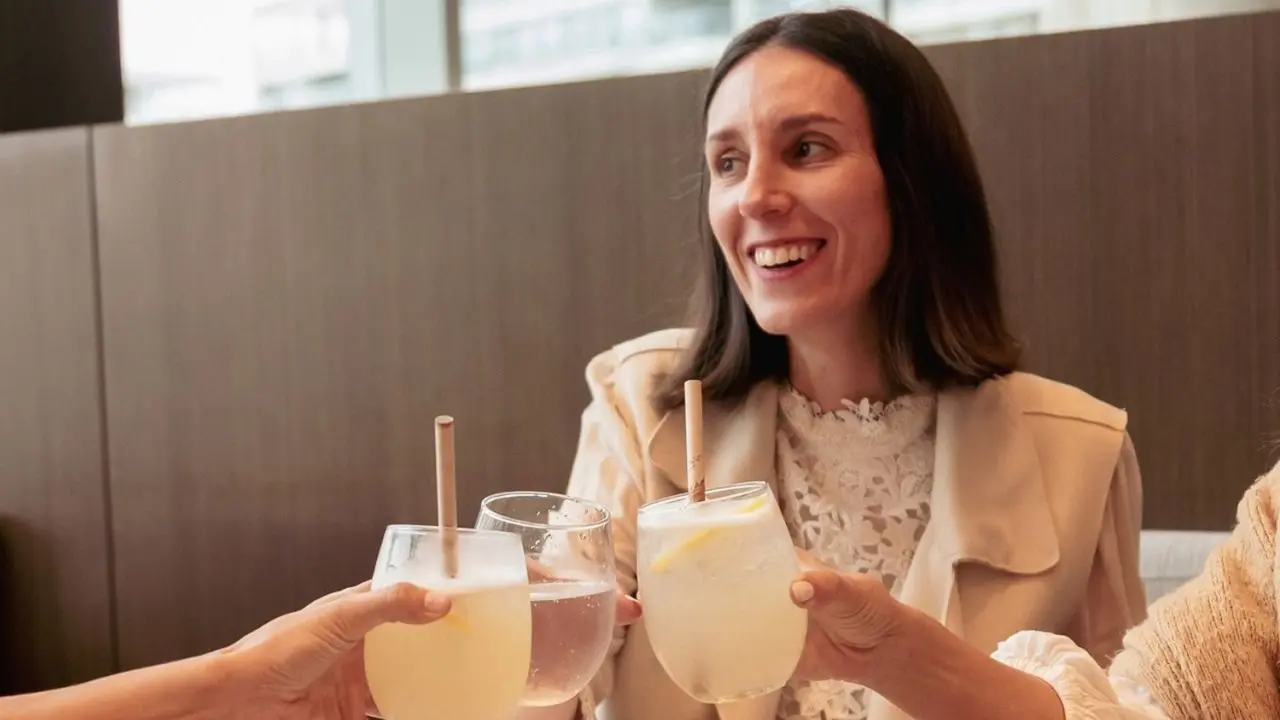 Una mujer sonriendo junto a otras mujeres a quienes solo se ven los brazos brindando
