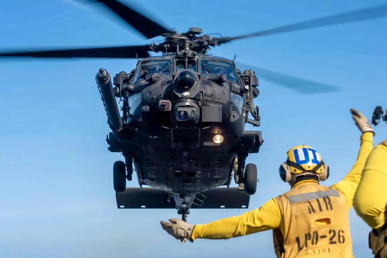 Un helicóptero militar Black Hawk en aproximación con dos operarios de pista de espaldas dando indicaciones con trajes amarillos