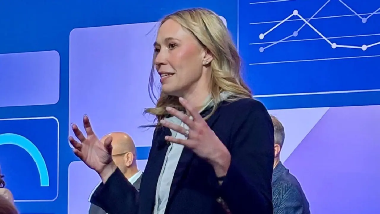Rebecca Carr, líder de HCM Products en SAP en un escenario dando una charla con una pantalla en tonos azules de fondo