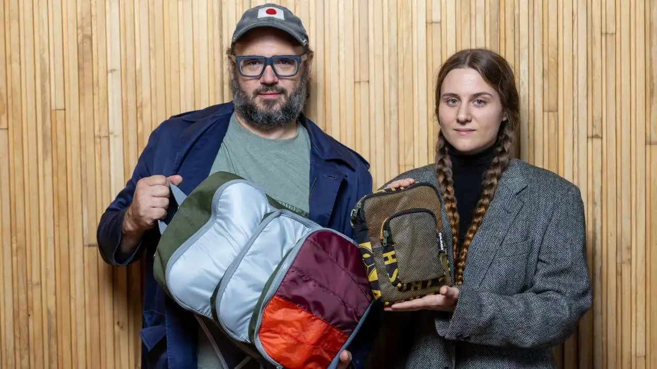 Un joven y joven mostrando las mochilas de la marca BAUMM fabricadas a partir de paracaídas en desuso