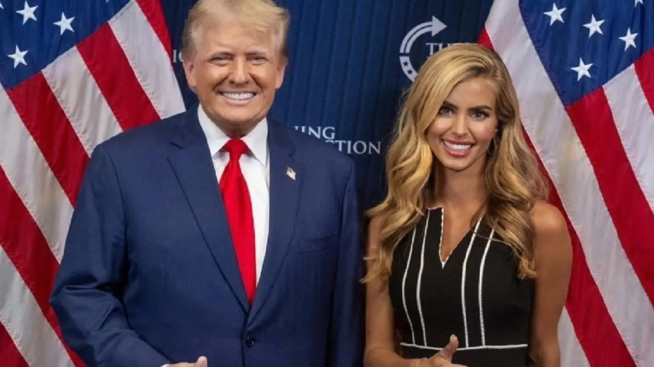 Donald Trump parado al lado de Katie Zacharia con banderas de EE.UU. al costado de cada uno