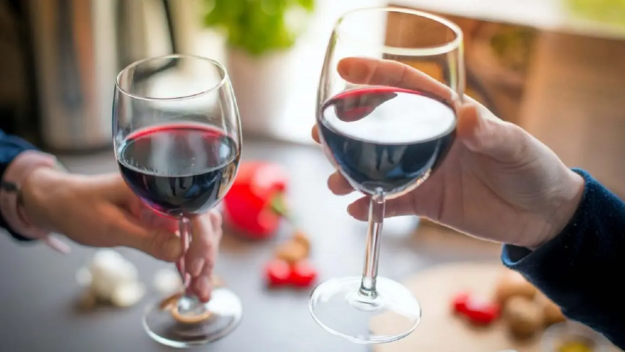 Dos manos teniendo cada una una copa de vino tinto y debajo una mesa
