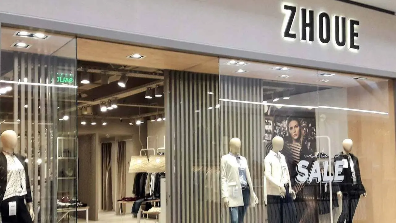 Local de ropa Zhoue, letras negras iluminadas sobre cartel gris. Vidriera con maniquíes