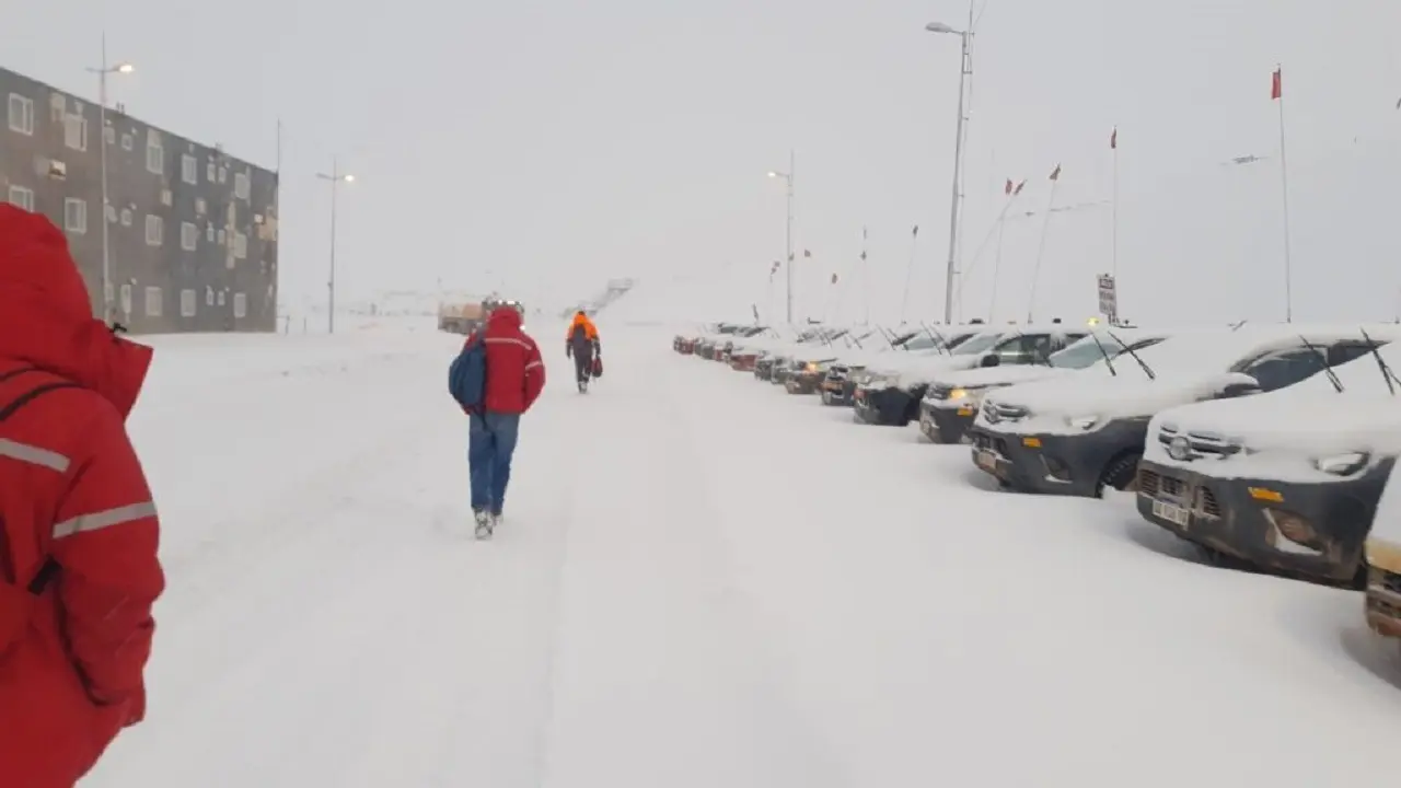 Hombres caminando alejados en la nieve y en el costado autos y camionetas estacionados cubiertos de nieve