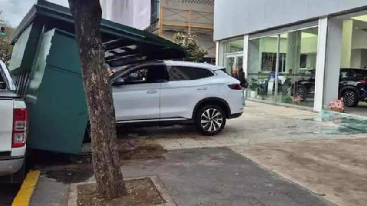 Auto SUV 0km color blanco chocado en la vereda contra un kiosco color verde y una concesionaria atrás