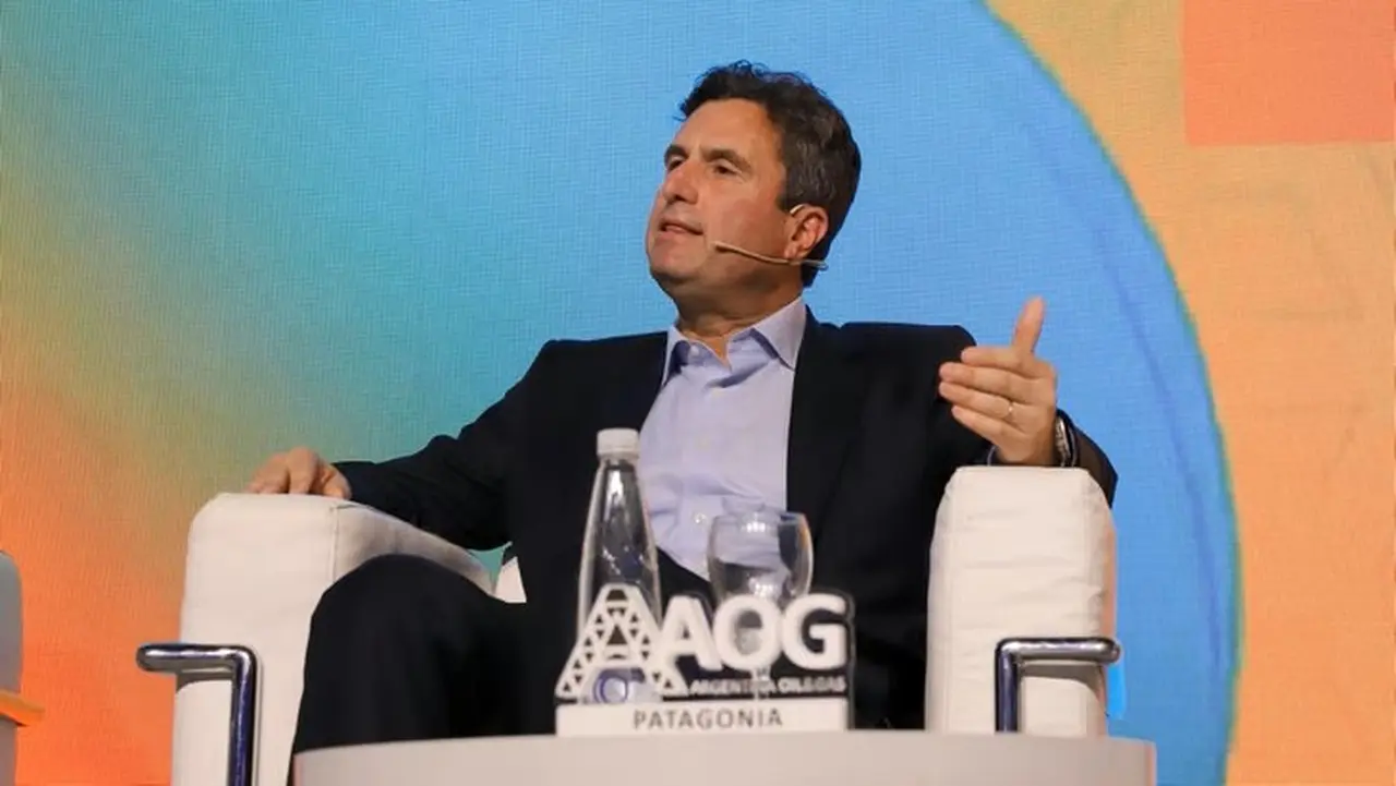 Julián Escuder CM de Pluspetrol sentado en un sillón blanco vestido de traje y con un fondo de una pantalla en naranja y celeste