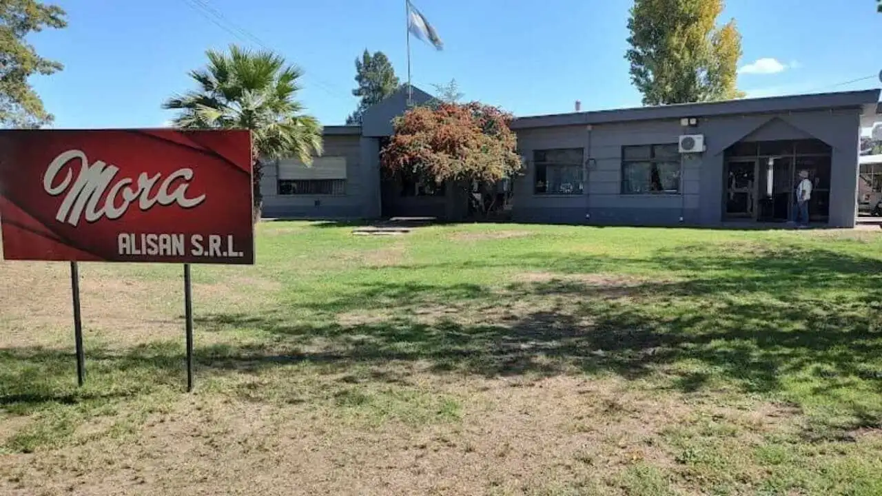 Planta Alisan SRL Mora. Cartel rojo con letras blancas sobre cesped