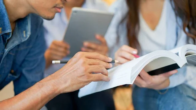 Grupo de estudiantes universitarios estudiando con libros, apuntes, lápices y una tablet en una mesa foto de archivo proveniente de banco de imágenes