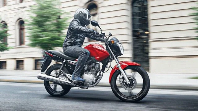 Un hombre con un casco andando en una moto roja. Imagen de archivo