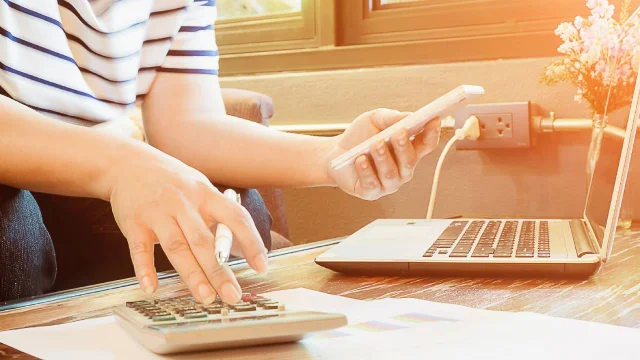 una persona haciendo cuentas con un celular, computadora y calculadora