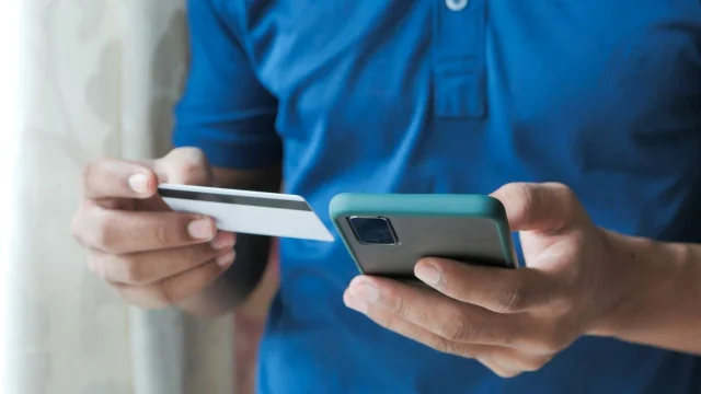 Persona con una tarjeta de un banco y un celular con una billetera virtual