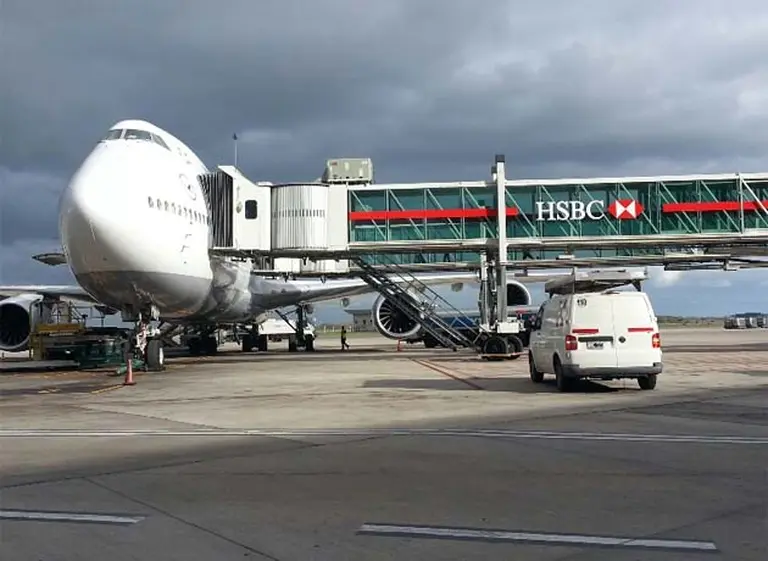 Un avión en la písta de un aeropuerta con la manga desplegada donde se ve la publicidad del banco HSBC