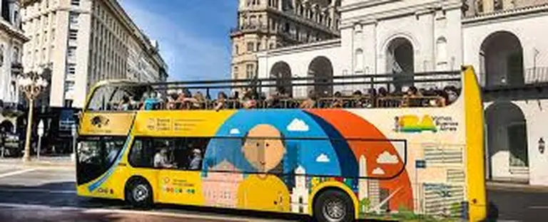 Un bus turístico de dos pisos con la parte de arriba descubierta paseando con personas en su interior por la ciudad de buenos aires