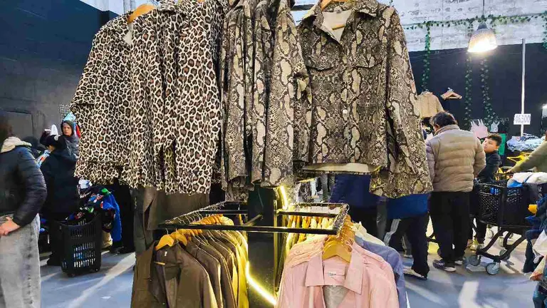 camisas y abrigos en galpón grande con gente haciendo fila para comprar