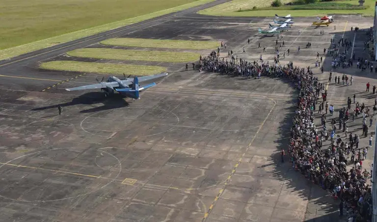 Vista aérea de la pista en la Base Aeronaval Punta Indio con un avión militar en maniobras y una multitud observando tras la línea de seguridad.