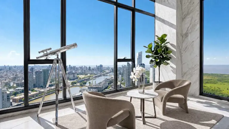 Living con sillones y mseita y un telescopio en nueva torre con amplias vistas a Puerto Madero en un día soleado