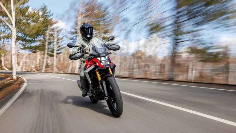 Un motociclista en una moto F450 GS de BMW anda por una ruta con arboles y cielo celeste que se ve por detrás y los costados