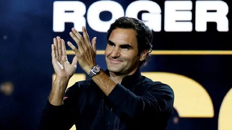 El extenista Roger Federer aplaudiendo delante de un fondo en el que hay un cartel con su nombre. 