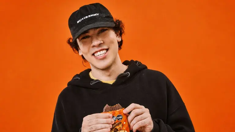 Joven vestido de negro sosteniendo un alfajor Giga con sus manos en un fondo naranja 