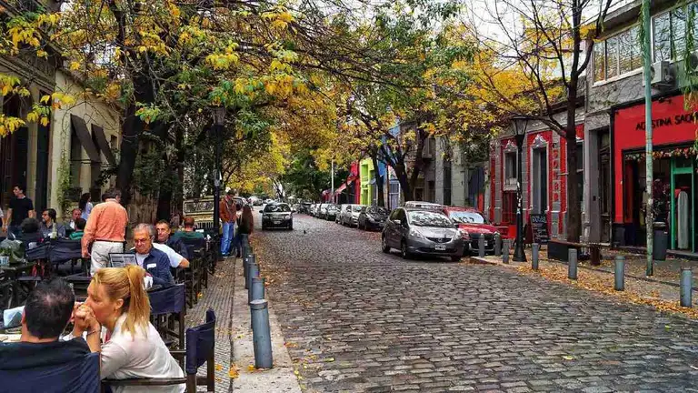 Calle empedrada de Palermo con personas sentadas en mesas en la vereda de un bar