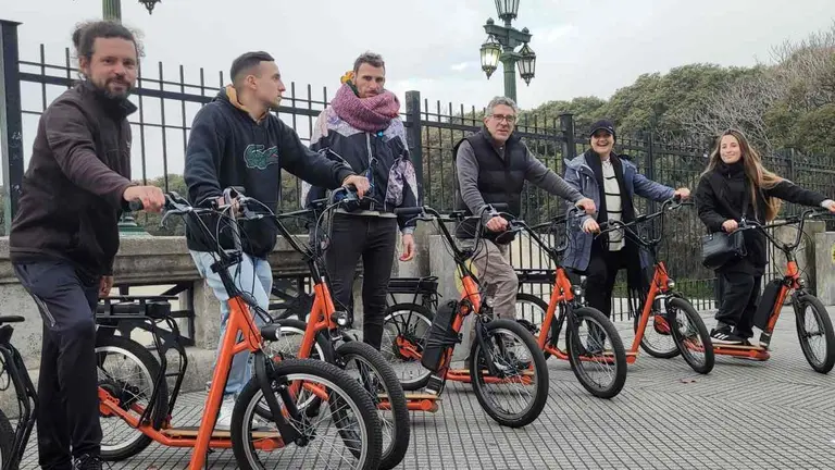 Grupo de 6 turistas arriba de bicipatinetas color naranja en un espacio público de la ciudad de buenos aires