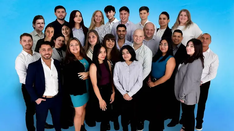 Un grupo de hombres y mujeres ubicados en varias filas y columnas vestidos como si estuvieran en una oficina. Todo sobre un fondo celeste 
