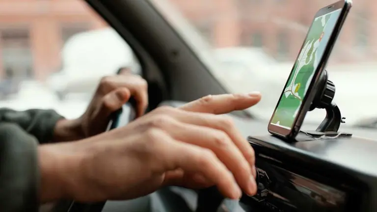 Una mano sobre un volante y otra señalando un celular con un mapa