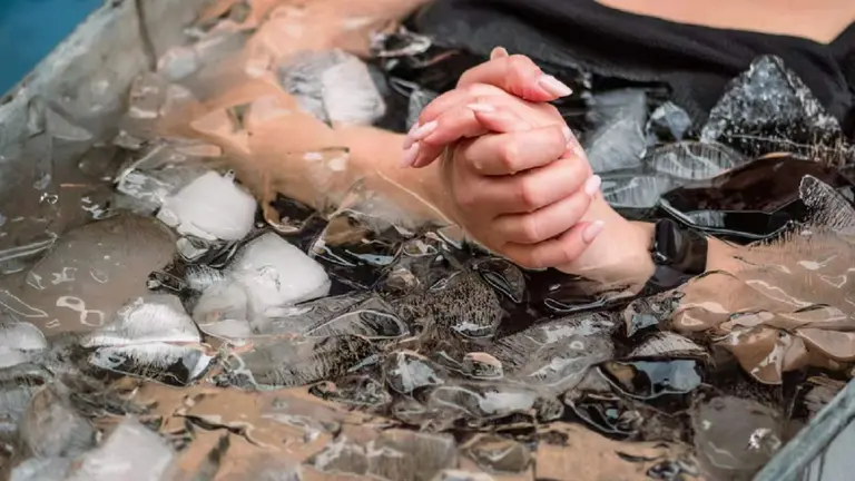 Dos manos de una mujer apretánsode y el resto del cuerpo que se ve en una tina con hielo y agua helada