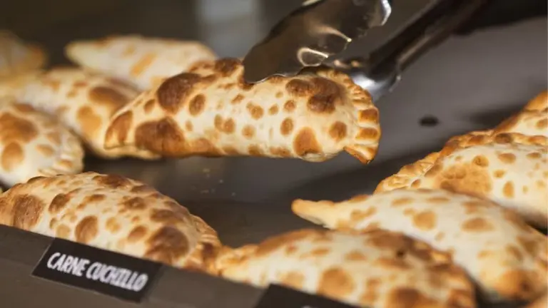 Una persona sirviendo empanadas con una pinza. 
