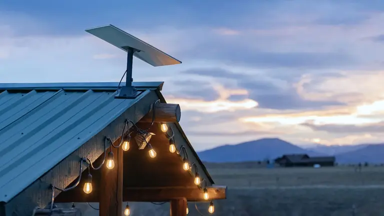 Antena Starlink sobre el techo de una casa en el campo con montañas de fondo