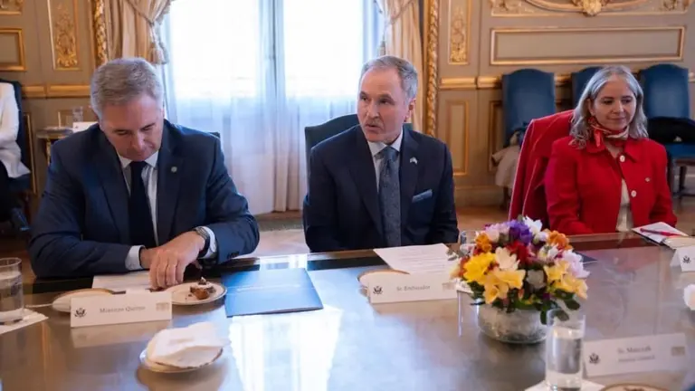 El ministro Quirnos y el embajador estadounidense Peter Lamelas en una mesa de madera con un florero de centro