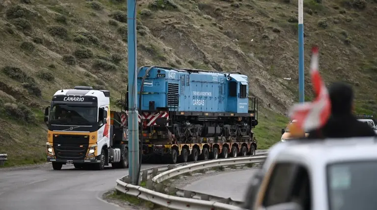 Un camión de carga pesada lleva un vagón de tren a través de una ruta con montañas en un costado