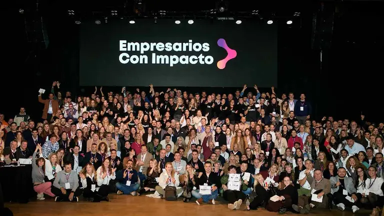Cientos de hombres y mujeres posando para una foto en un salón con una pantalla atrás que dice 'Empresarios con Impacto'