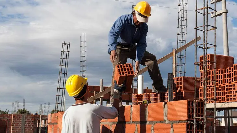 Dos trabajadores de la construcción se pasan unos ladrillos en una obra en construcción