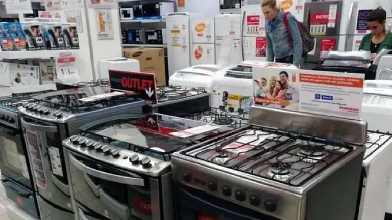 Negocio de electrodomésticos con varias cocinas en primer plano, heladeras y otros dispositivos por detrás y dos personas recorriendo el lugar