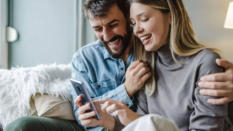 hombre y mujer sonriendo mientras miran un celular
