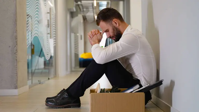 Un hombre sentado en el suelo, junto a una caja, parece abatido tras perder su empleo