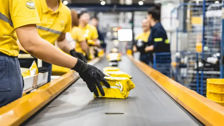 trabajador de mercado libre tomando una caja sobre una cinta embaladora 