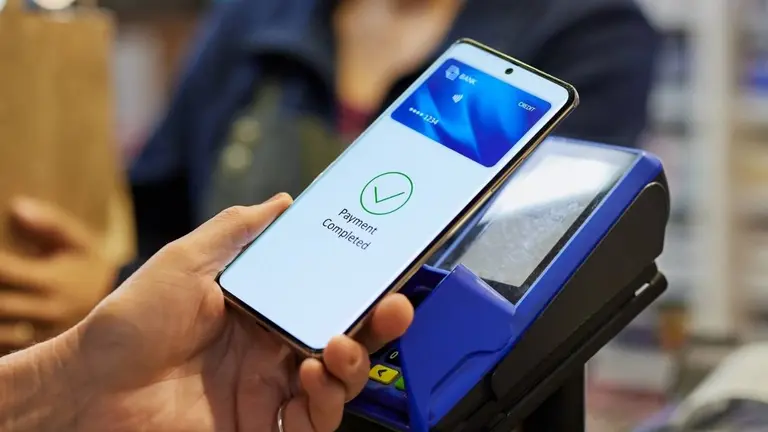 Usuario apoyando su celular en una terminal de cobro para pagar sin contacto con una billetera NFC