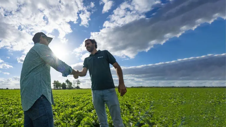 dos hombres sujetándose la mano en medio de un campo sembrado